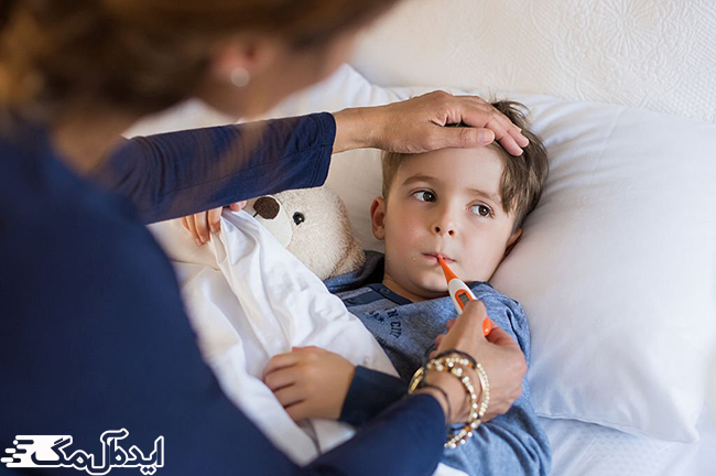 پسر بچه مبتلا به سرماخوردگی روی تخت خوابیده و مادر دمای بدن او را اندازه می‌گیرد
