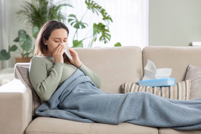زن مبتلا به بیماری سرماخوردگی روی کاناپه دراز کشیده است