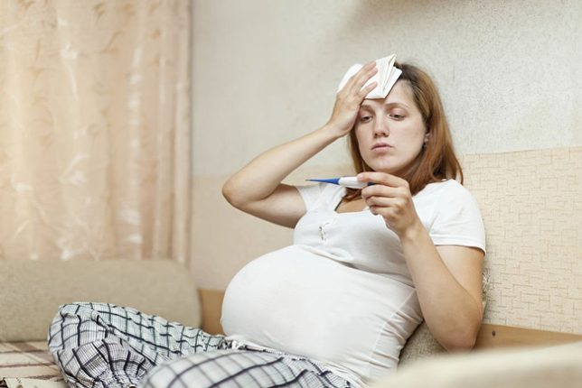 زن باردار مبتلا به سرماخوردگی با تب‌سنج دمای بدن خود را اندازه می‌گیرد
