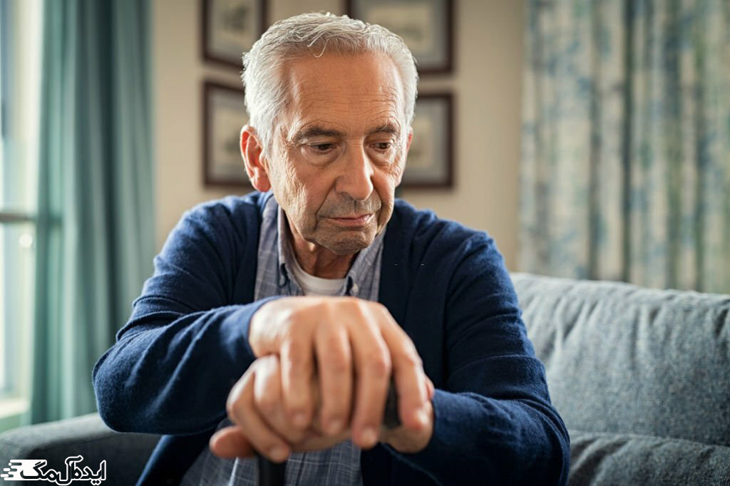 مرد سالمند روی مبل نشسته و دست‌ها را روی عصا قرار داده است