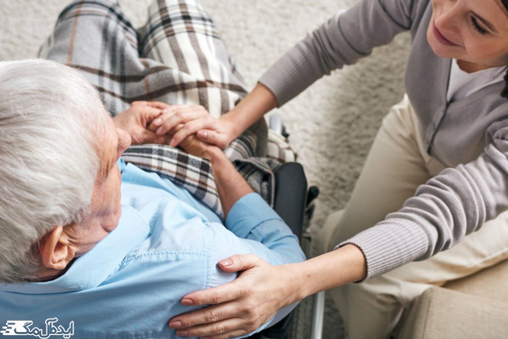 یک مرد سالمند روی ویلچر نشسته و پرستار او دست خود را روی شانه او گذاشته است