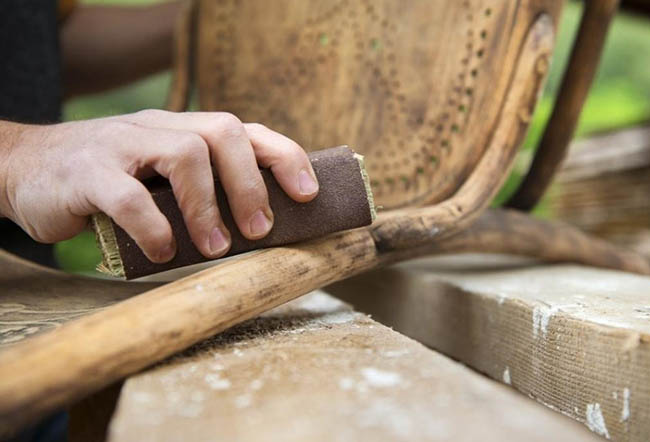 یک نفر در حال سمباده زدن دسته صندلی چوبی است