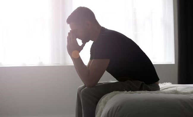 یک مرد افسرده روی تخت نشسته و صورتش را با دست گرفته است
