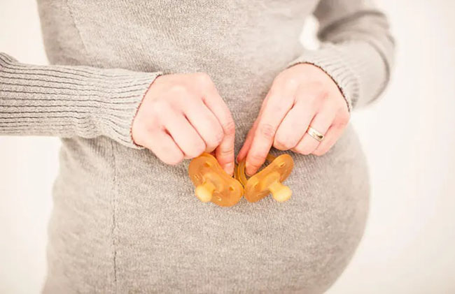 یک زن باردار که دو پستانک را جلوی شکم خود نگه داشته است