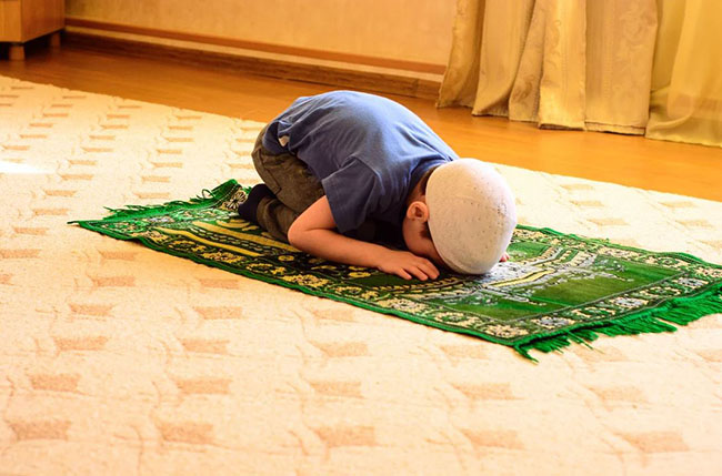 یک کودک در حال نماز خواندن روی سجاده