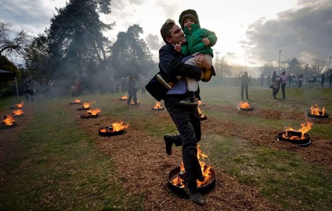 یک مرد، فرزند خود را در آغوش گرفته و در مراسم چهارشنبه سوری از روی آتش می پرد